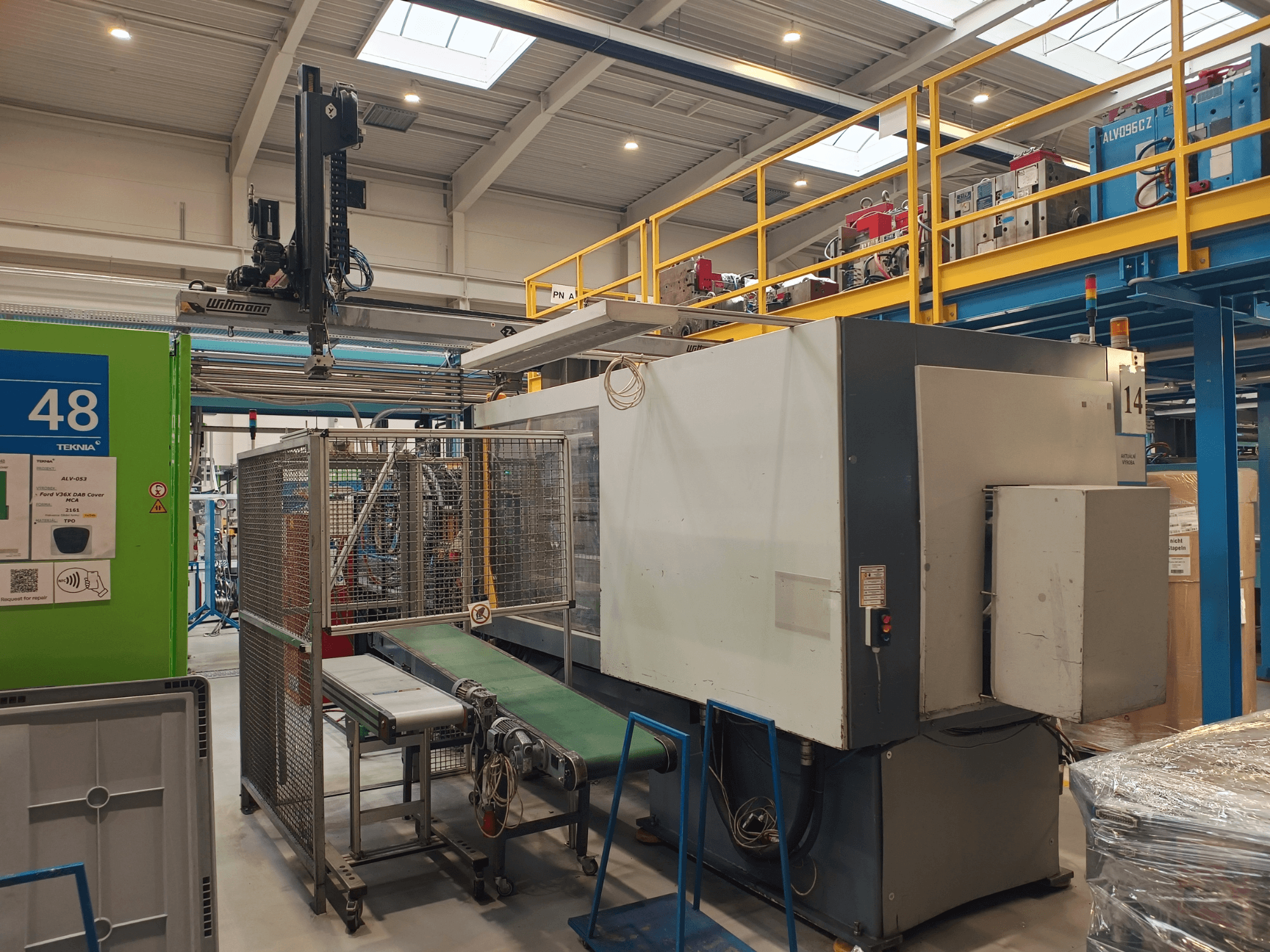 Industrielle Automatisierungsausrüstung mit grünem Förderband, beschriftet mit '48', und Brückenkran; Seitenansicht der Maschine in der Fabrikhalle.